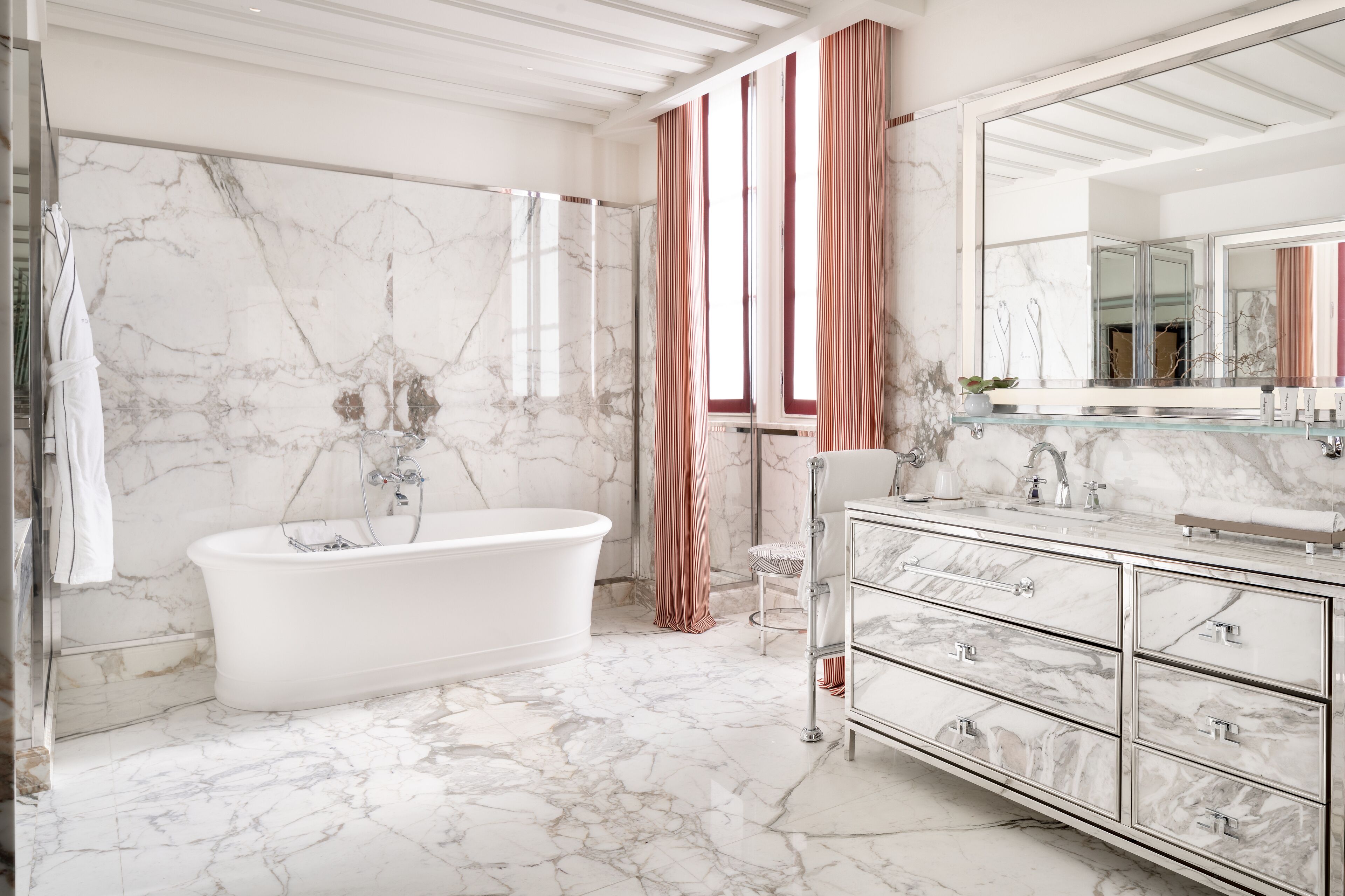 Une salle de bain avec une baignoire îlot, des murs en marbre, un grand miroir et un meuble-lavabo moderne dot é de tiroirs.