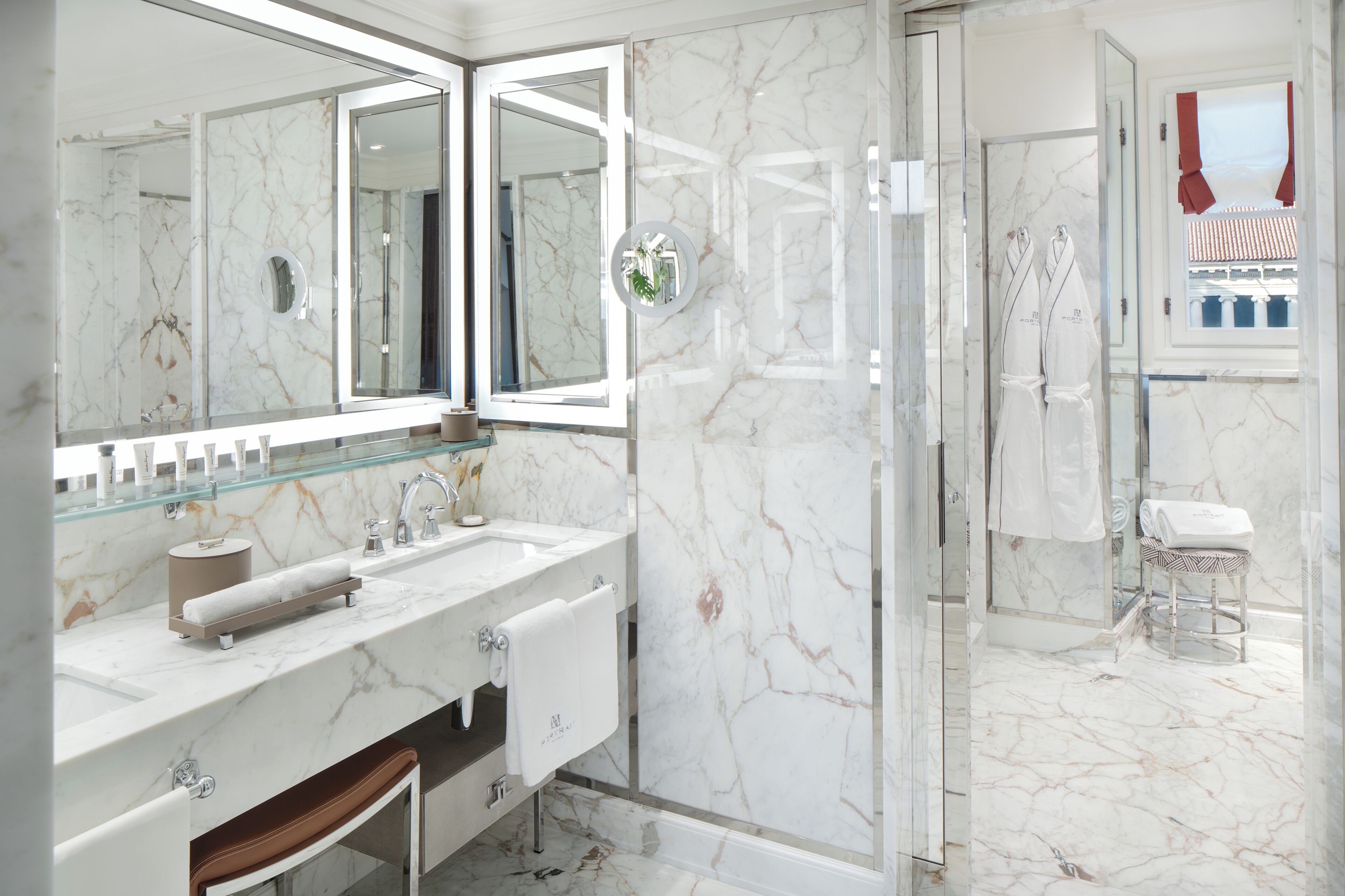 A modern bathroom with a glass shower enclosure, a marble-tiled floor, and a large mirror above the sink.