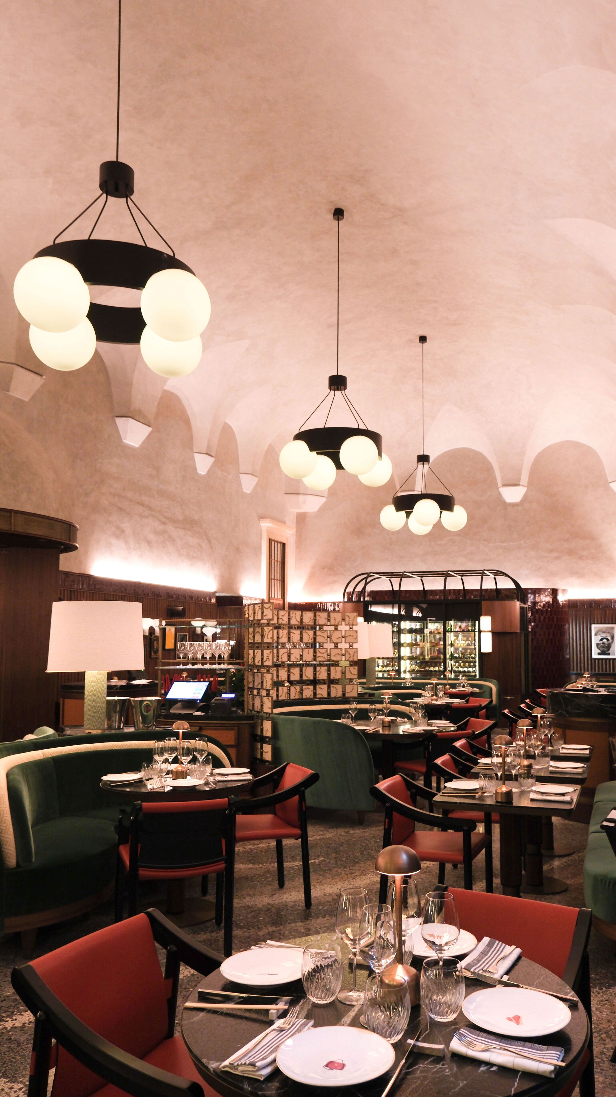 Een restaurant met ronde tafels, rode stoelen en hangende sferische lampen.