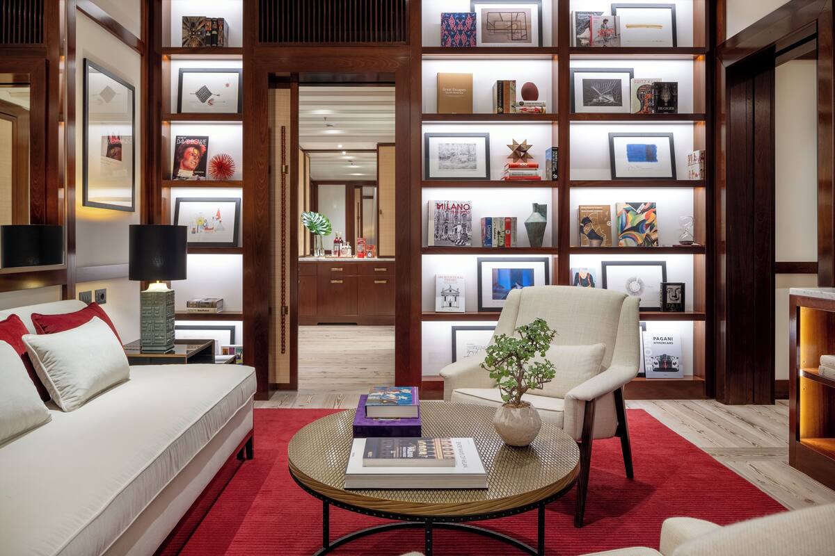 A modern living room with a sofa, armchair, and coffee table, featuring a bookshelf with various framed items and a potted plant.