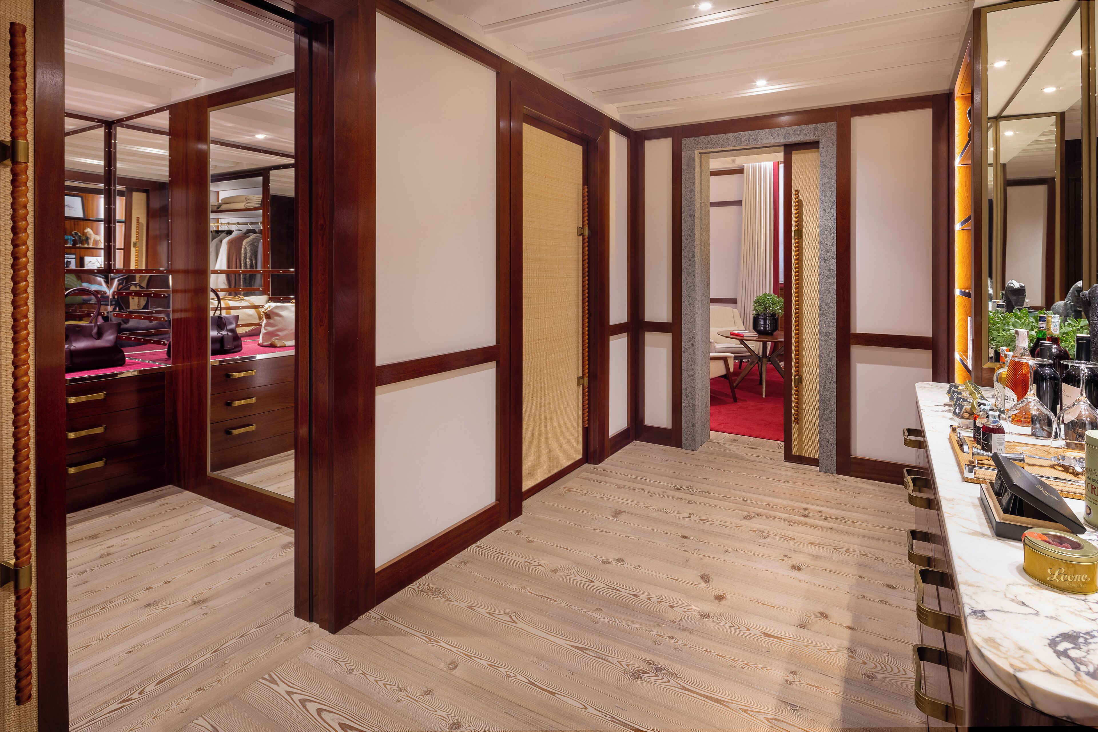 A hotel room with a wooden floor, a large mirror, a vanity with toiletries, and a red carpet leading to a dining area.