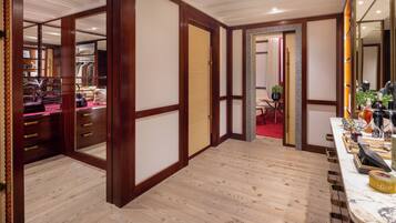 A hotel room with a wooden floor, a large mirror, a vanity with toiletries, and a red carpet leading to a dining area.
