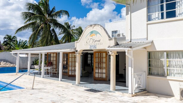 Una propiedad frente a la playa llamada "El Retreat", con piscina, palmeras y un patio cubierto.