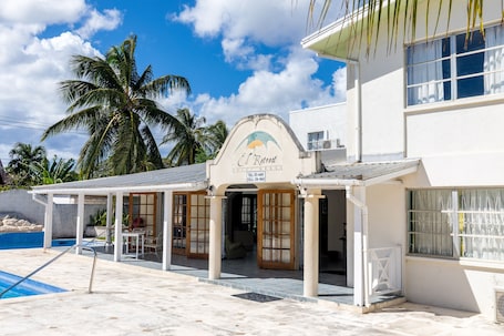 A beachfront property named "El Retreat" with a pool, palm trees, and a covered patio area.