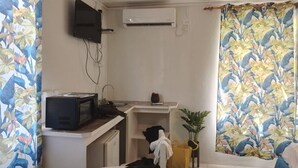 Habitación de hotel compacta con cama, un pequeño escritorio con televisor, aire acondicionado en la pared y una ventana con cortinas florales.