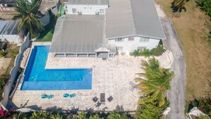Vista aérea de una casa con piscina, mobiliario de patio y abundante vegetación.