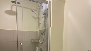Moderni kylpyhuone, jossa on lasiseinällä varustettu suihku, valkoinen wc-istuin ja pesuallas.