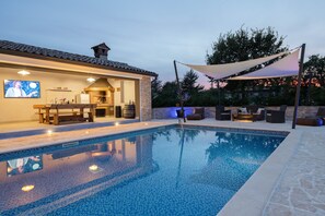 A swimming pool with a stone deck, a barbecue area, and outdoor seating.