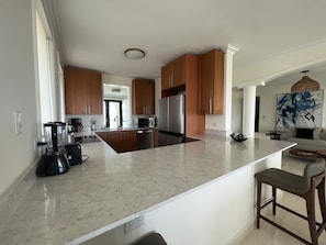 Una cocina moderna con armarios de madera, una isla grande, electrodomésticos de acero inoxidable y vistas al área de estar.