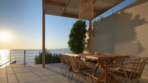 Een terras met een houten tafel en stoelen, een hanglamp en uitzicht op zee.