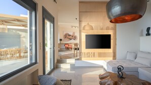 Een moderne woonkamer met een grote televisie, een witte bank en een eethoek met stoelen en een tafel.