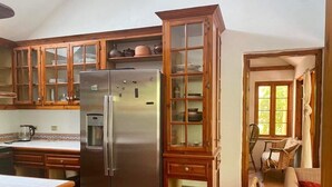 Een keuken met houten kastjes, een roestvrijstalen koelkast, en een eethoek met een tafel en stoelen.