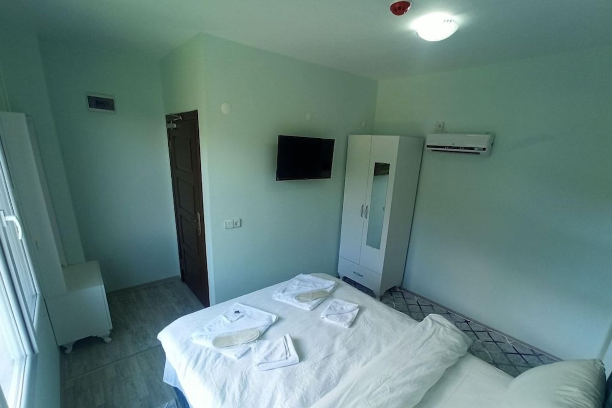 A hotel room with a bed, a wardrobe, a television, and an air conditioning unit.