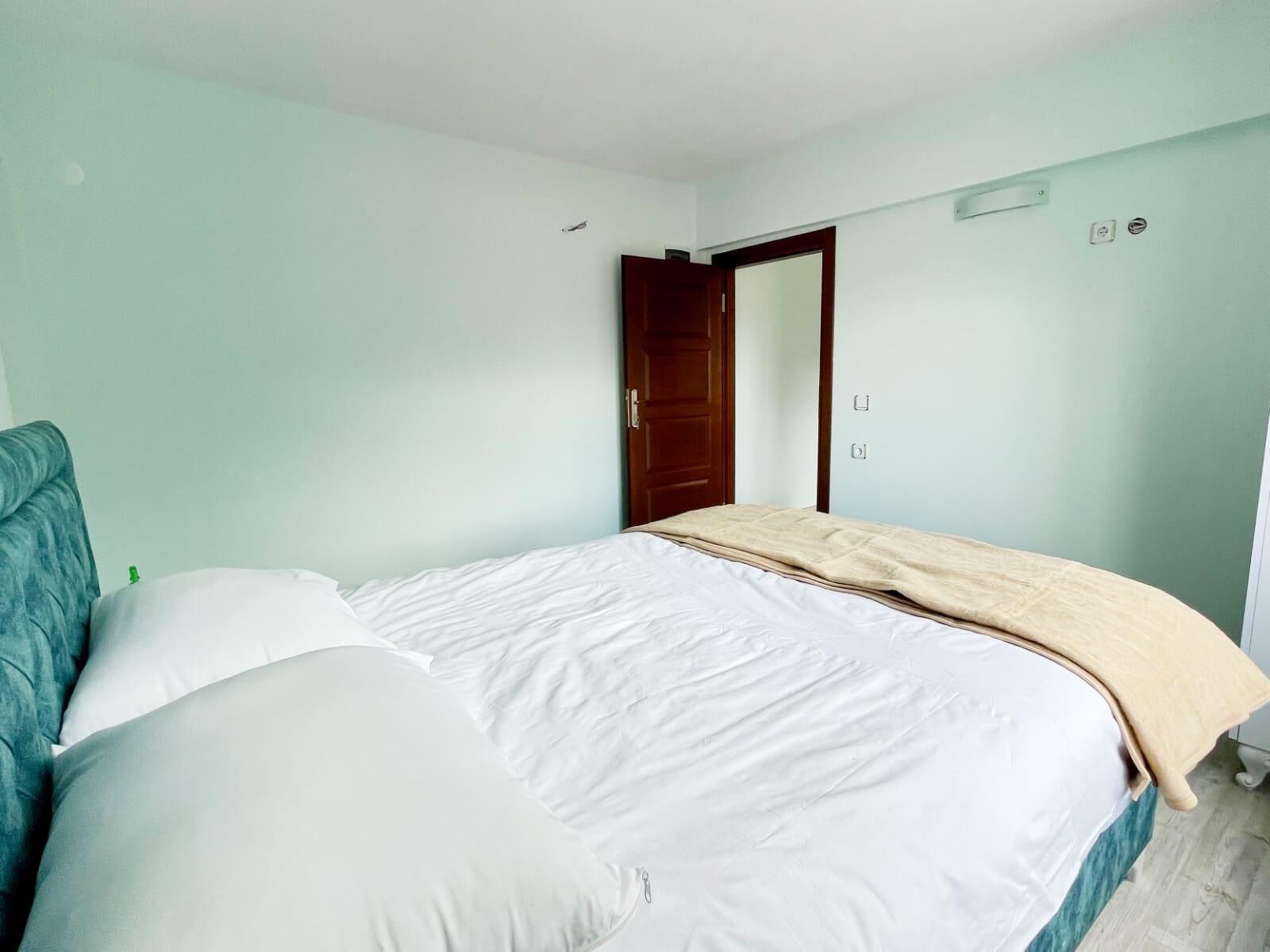 Quarto com cama, cabeceira azul, porta de madeira e paredes claras.