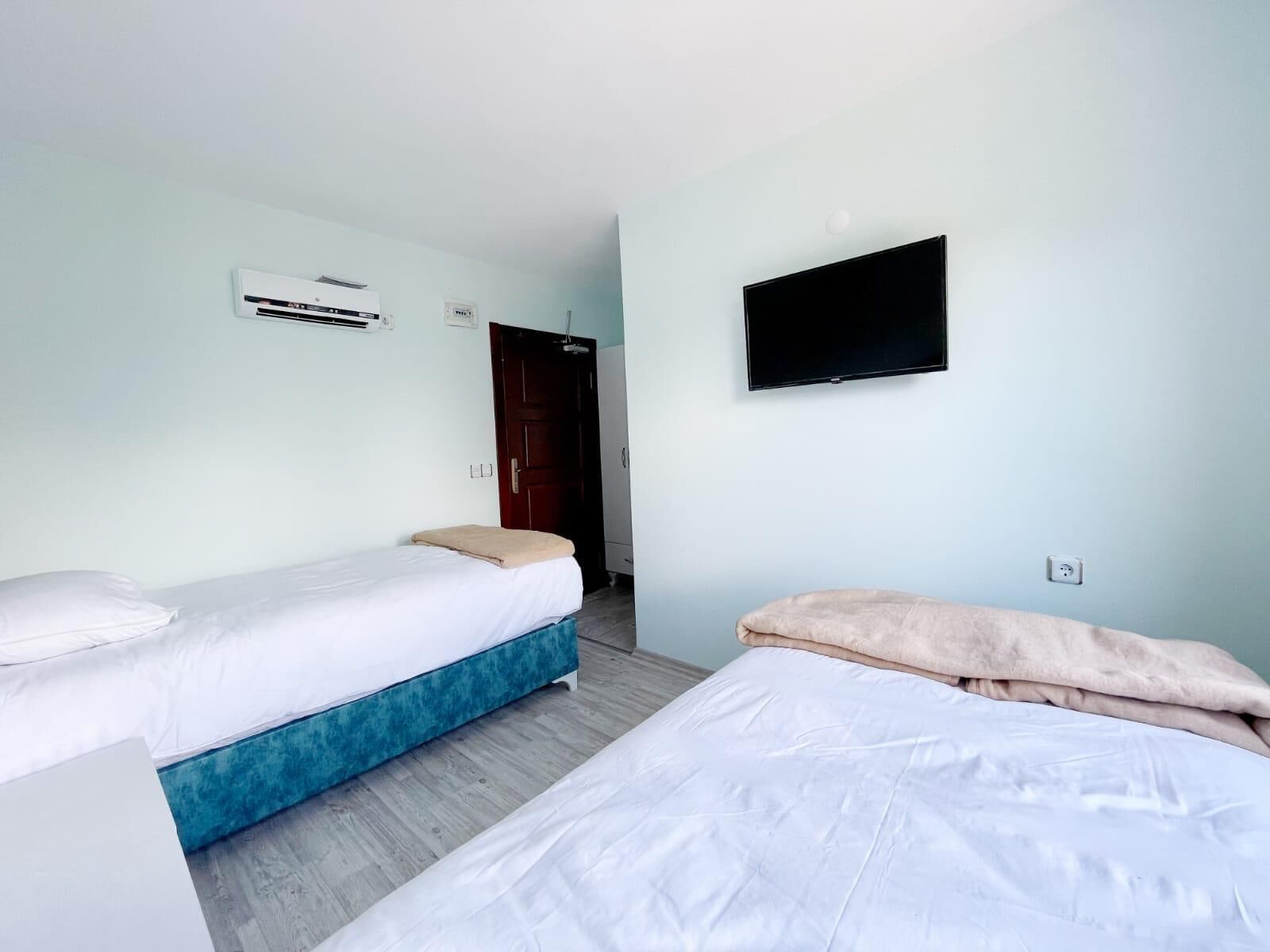 A room with two beds, a TV, an air conditioning unit, and a door.