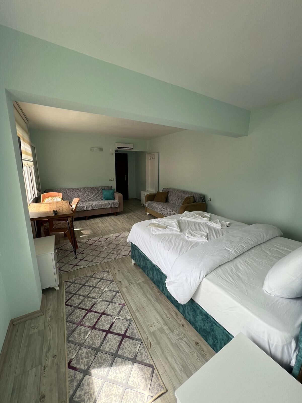 A hotel room with a large bed, two smaller beds, a desk, and a chair.