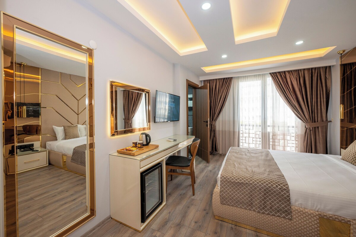 A modern hotel room with a bed, desk, chair, and a large mirror.