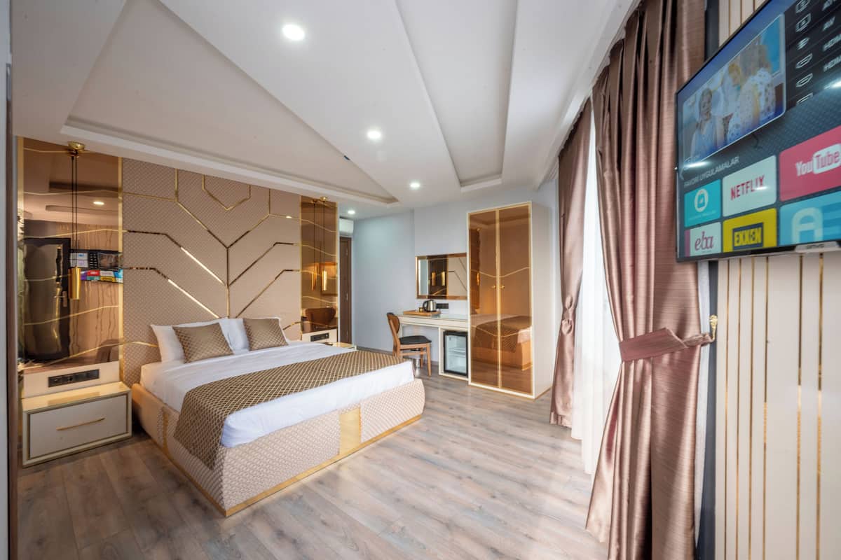 Ein modernes Hotelzimmer mit einem großen Bett, einem Schreibtisch und einem an der Wand befestigten Fernseher, der verschiedene Sender anzeigt.