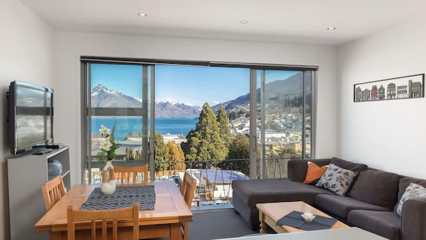 A modern living room with a large sliding glass door leading to a balcony with a scenic mountain and lake view. - Welcome to Ballarat Bungalow. A Chic Central Stay with Easy Access to Queenstown’s Best! (Queenstown)