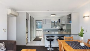 A modern kitchen with a central island, bar stools, and a dining table with a patterned table runner. - Welcome to Ballarat Bungalow. A Chic Central Stay with Easy Access to Queenstown’s Best! (Queenstown)