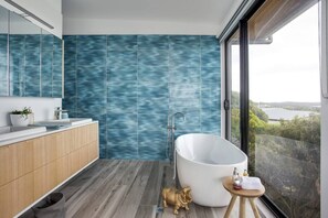 Bathroom features a bathtub, wooden vanity, and a large window offering a view of the outdoors.
