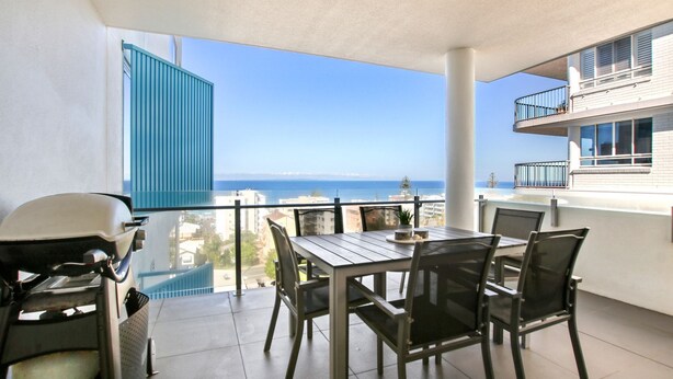 A balcony with a table and chairs, a grill, and a view of the sea and buildings. - Aquaview Unit 304, 29 Canberra Tce, Kings Beach (Kings Beach)