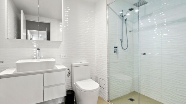 A modern bathroom with a glass shower enclosure, a white sink, and a toilet.