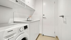 A compact laundry room with a Samsung washing machine, a small sink, and a door. - Aquaview Unit 304, 29 Canberra Tce, Kings Beach (Kings Beach)