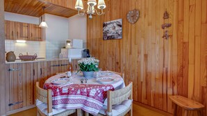 A wooden-paneled room with a dining table set for two, a chandelier, and a clock on the wall. - Les Marmottes du Morzena (Morzine)
