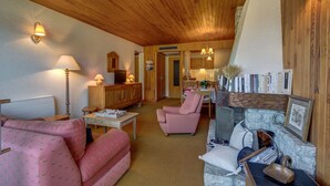 A cozy living room with a wooden ceiling, a television, a dining table with chairs, and a bookshelf filled with books. - Les Marmottes du Morzena (Morzine)