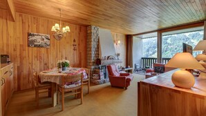 A cozy wooden interior with a dining area, a fireplace, and large windows offering a view of the outdoors. - Les Marmottes du Morzena (Morzine)