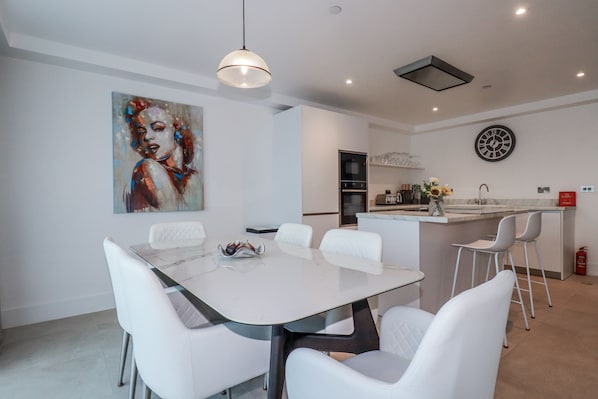 A modern kitchen with white cabinetry, a central island with bar stools, and a dining area with a white table and chairs.