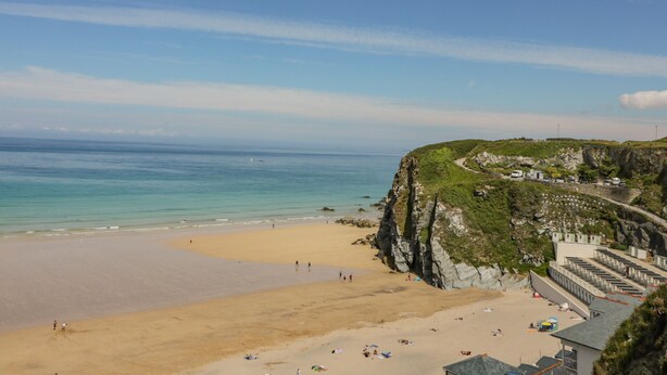 A beach with a rocky cliff and a row of beach huts. - 13 Cliff Edge (Newquay)