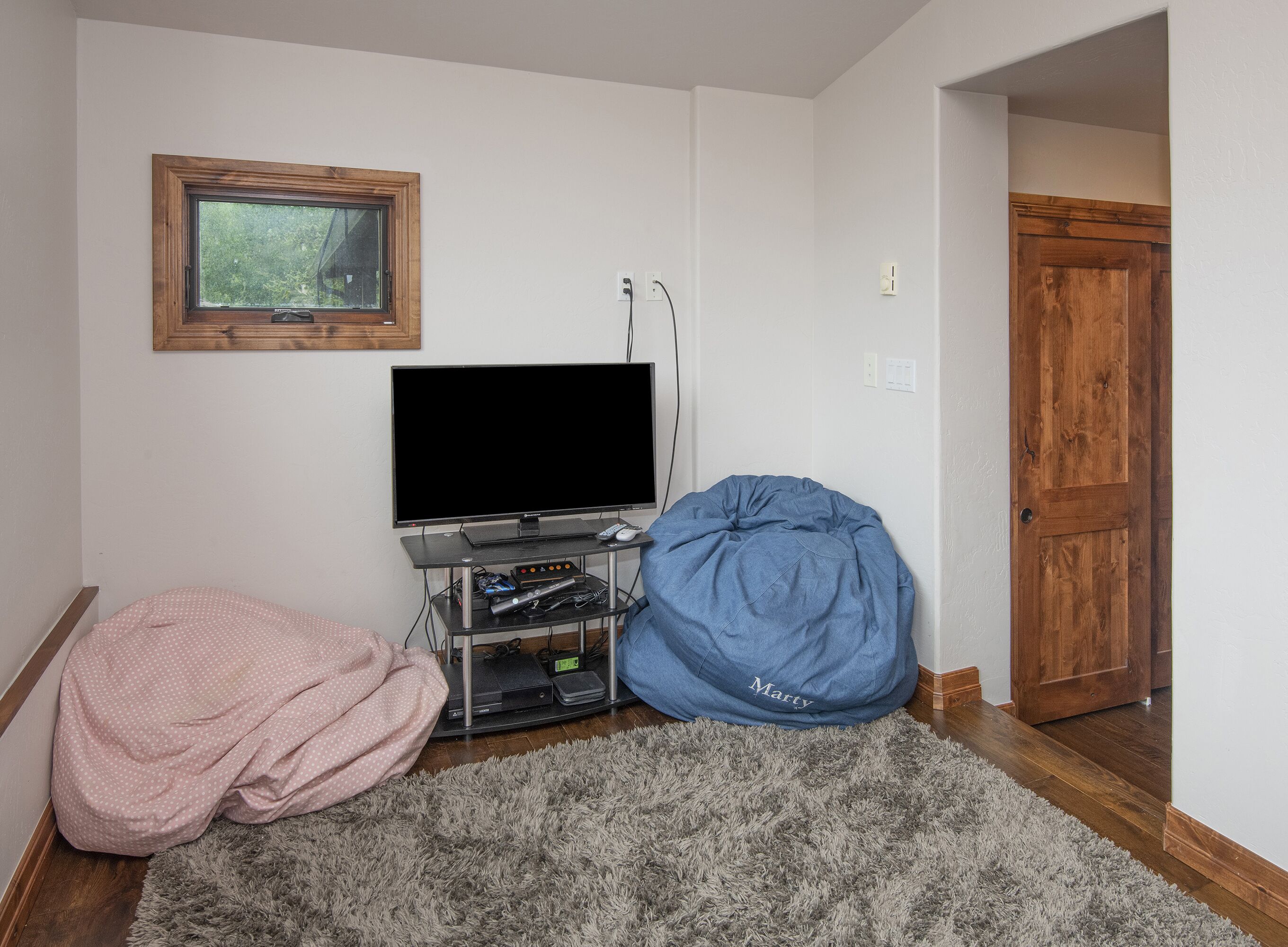 A room with a television on a stand, a blue bean bag chair, and a pink polka-dotted blanket on the floor.