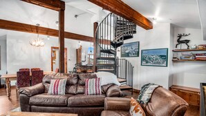 A spacious living room with a brown leather sofa, a wooden coffee table, and a spiral staircase. - Luxurious condominium in Perfect Location on Bridge Street, Near Gondolda 1!! (Vail)