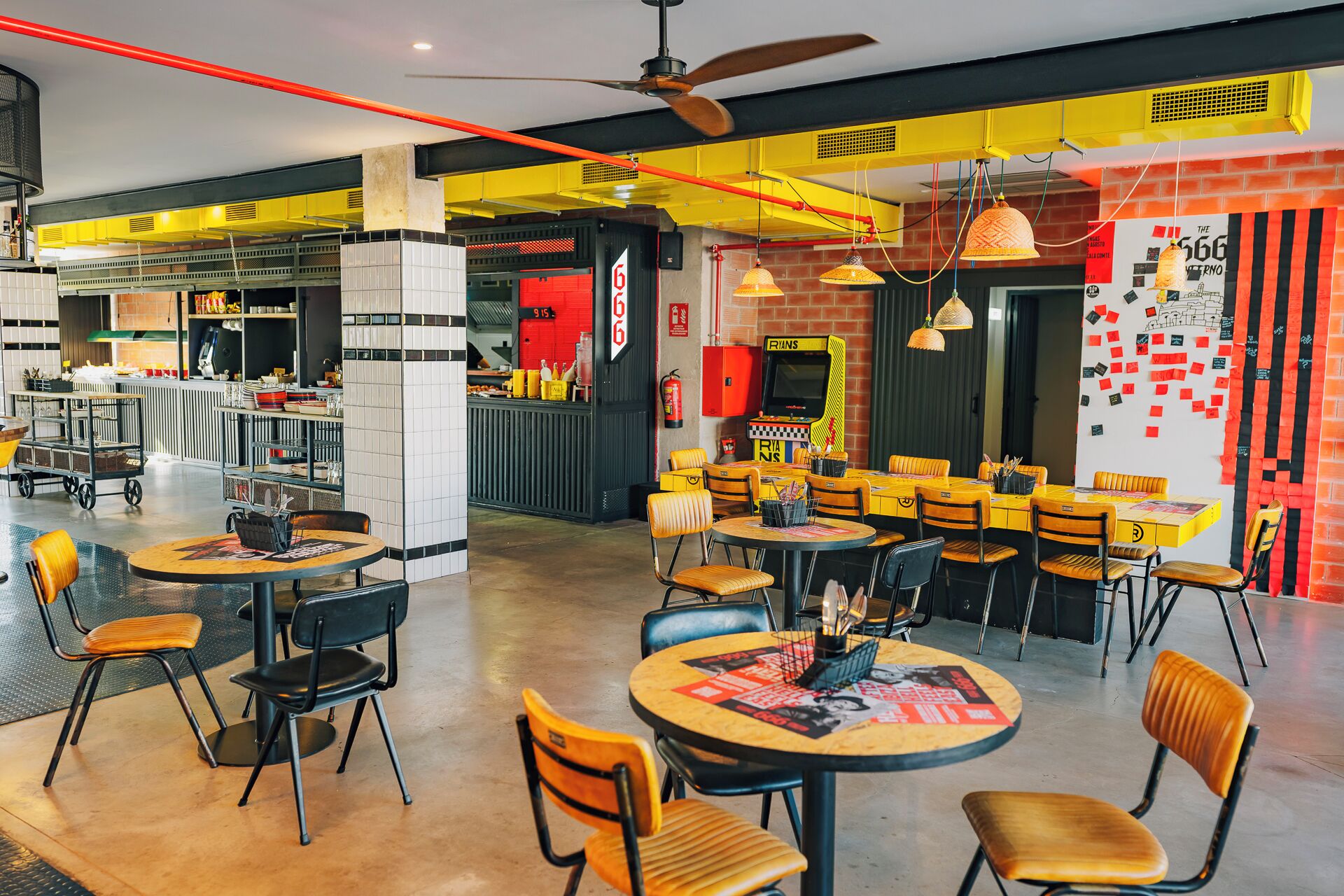 A restaurant with multiple tables and chairs, a kitchen area, and a wall with a game machine.