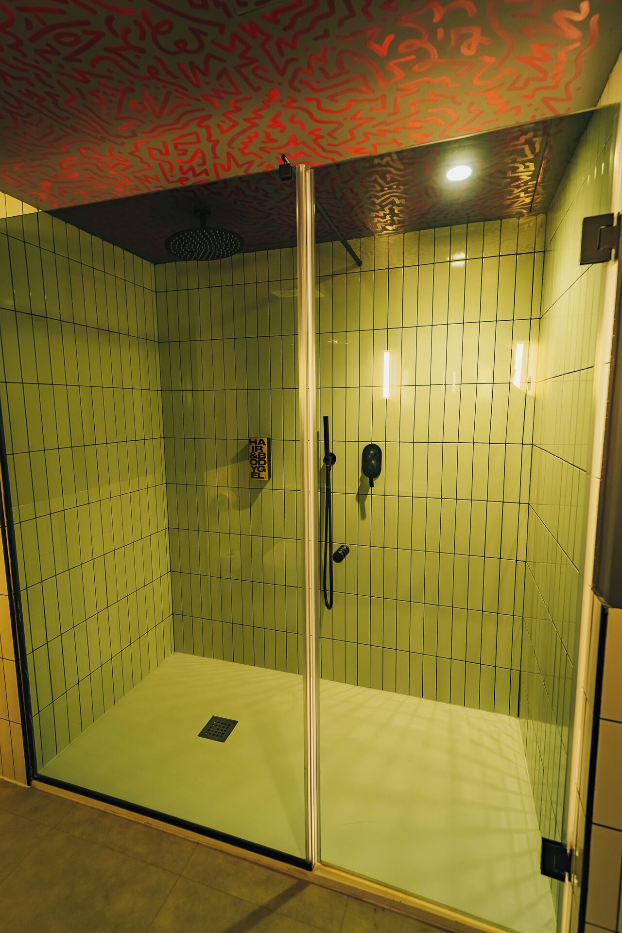 Ducha envuelta en vidrio con pared de azulejos, cabezal de ducha de mano y masajeadora manual.