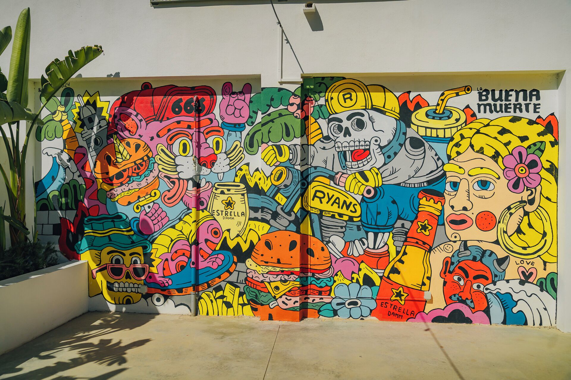 A colorful mural with various characters and objects, including a skull, a flower, and a sign that says 'BUENA MÚERTE'.