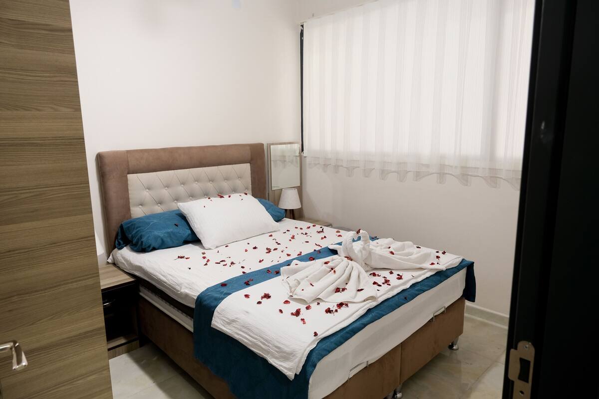 A neatly made bed with a blue and white bedspread, a wooden headboard, and a bedside table with a lamp.