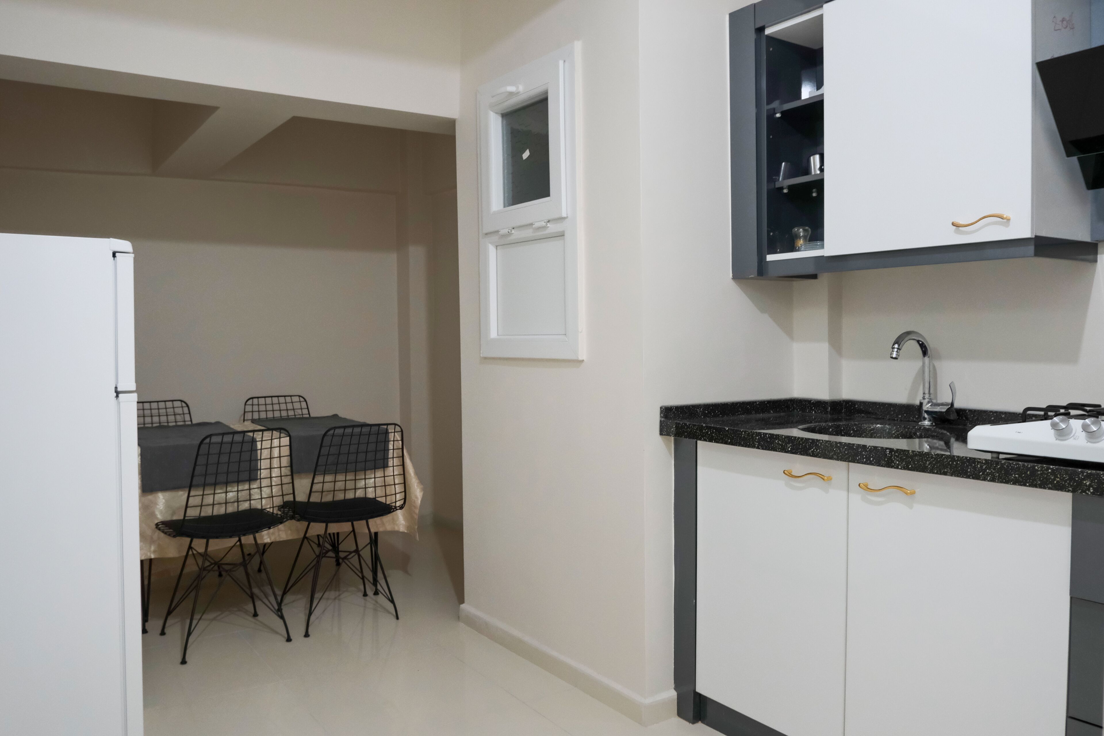 A compact kitchen with white cabinets, a black countertop, and a window above the sink.