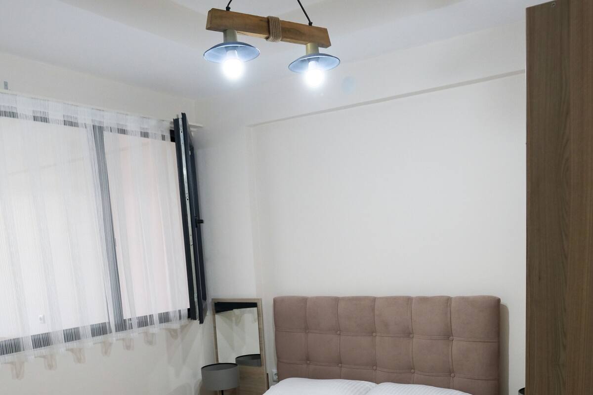 A bedroom with a bed, bedside tables, a mirror, and a ceiling light fixture.
