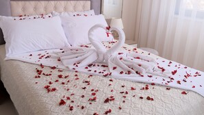 A neatly made bed with a heart-shaped towel arrangement and scattered rose petals. - Merkür Hotel (Ihsaniye)