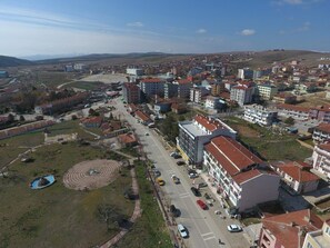 An aerial view of a town with a mix of residential and commercial buildings, a central road, and a circular park area. - Merkür Hotel (Ihsaniye)
