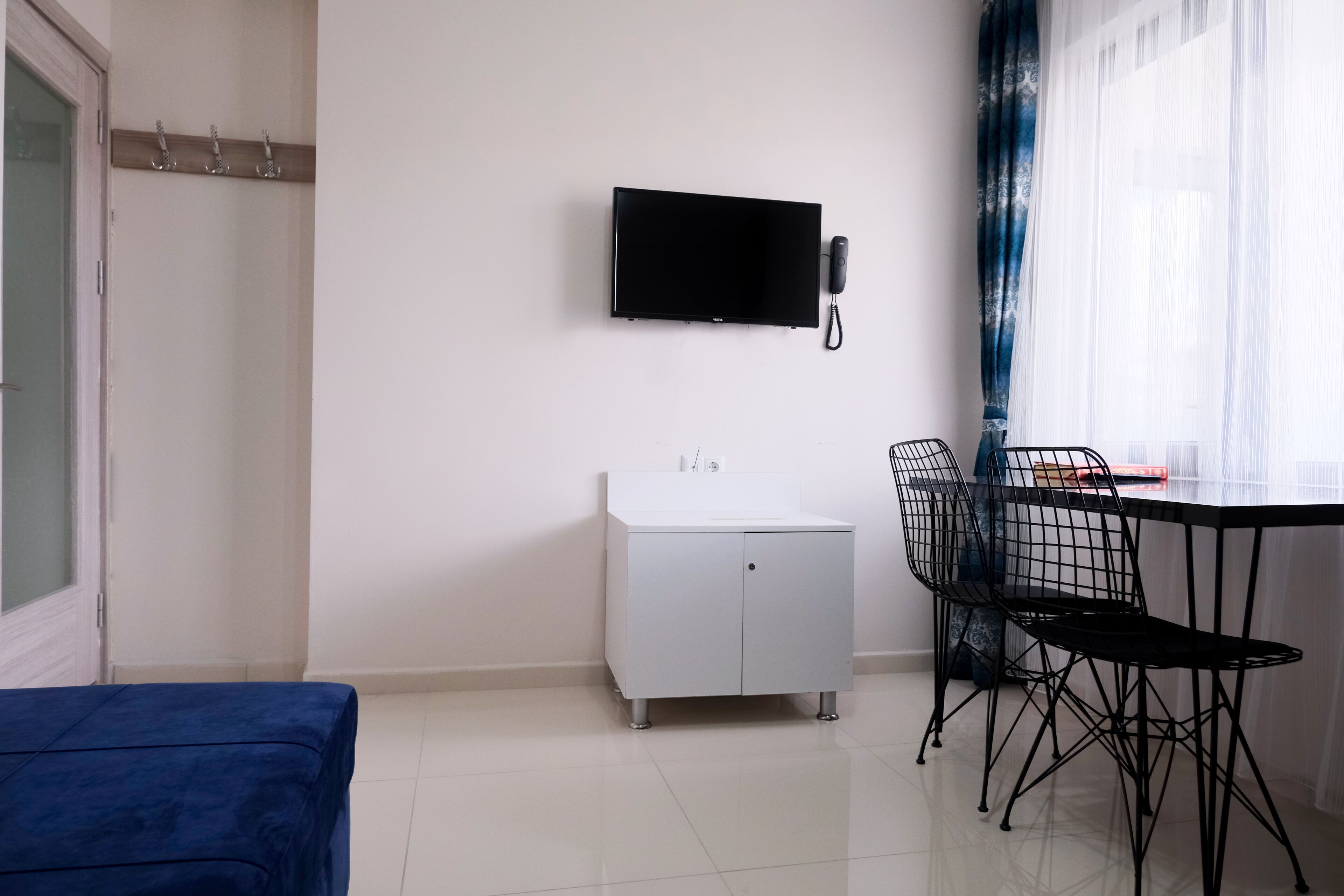 A hotel room with a bed, a desk with a chair, a TV mounted on the wall, and a small cabinet.