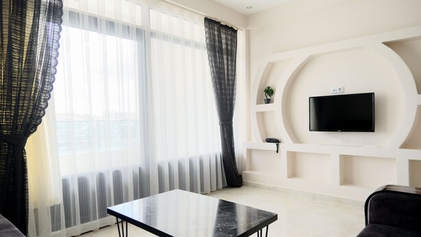 A modern living room with a black table, a sofa, and a TV mounted on a white wall. - Merkür Hotel (Ihsaniye)