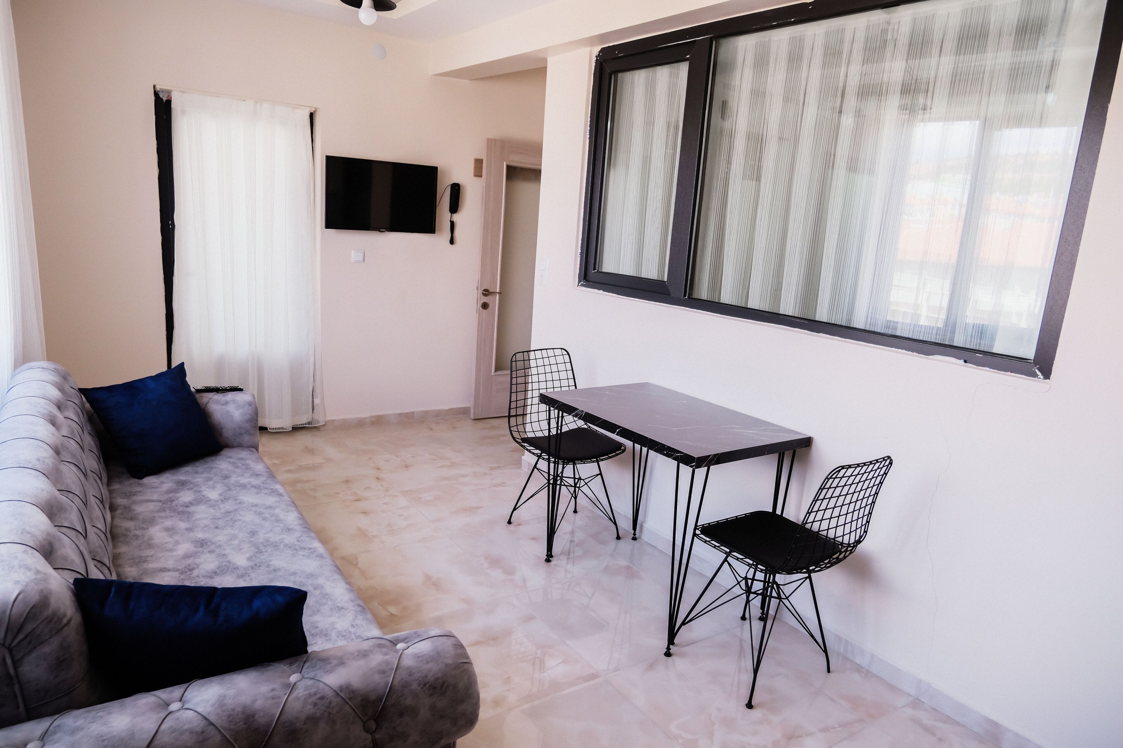 A living area with a sofa, two chairs, a small table, a TV, and a window with curtains.