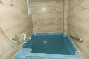 A bathroom with a blue-tiled bathtub, a shower area, and a marble wall. - Merkür Hotel (Ihsaniye)