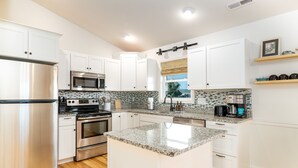 Una cocina moderna con armarios blancos, electrodomésticos de acero inoxidable, encimeras de granito y un ventanal con vistas.