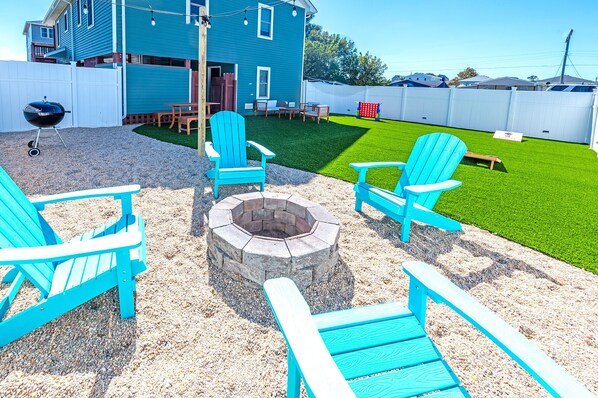 A backyard with a fire pit, blue Adirondack chairs, a wooden table, and a white fence. - Coastal escape, steps away from the waves! (Kill Devil Hills)