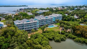 A multi-story hotel with a pool, surrounded by dense greenery and a body of water. - The Skimmer Condo: Downtown on the Bay - Nature Views - Bird watching (Cedar Key)